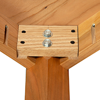 Detailed view of a wooden table showing leg attachment with use of two screws.