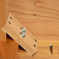 Detailed view of a wooden table showing leg attachment with use of two screws.