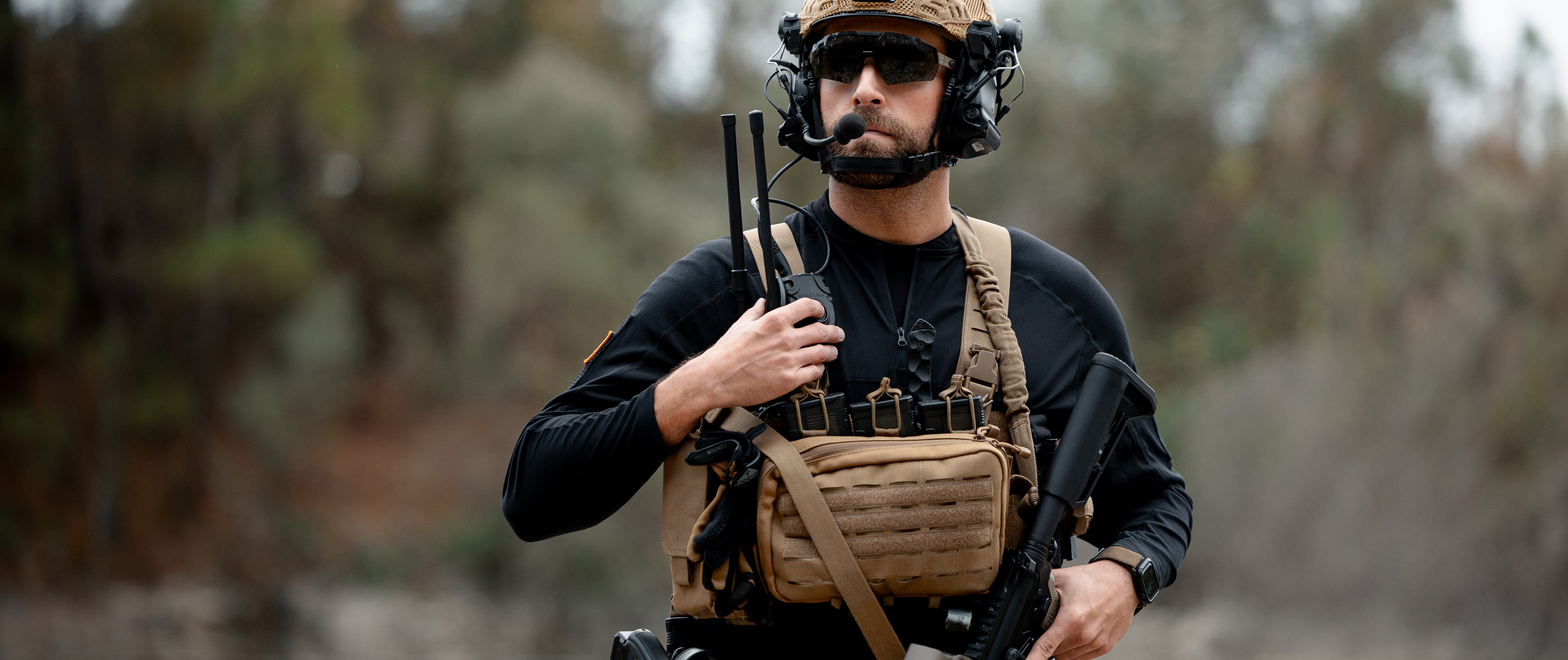 man in a chest rig using his radio while wearing a trident battle top