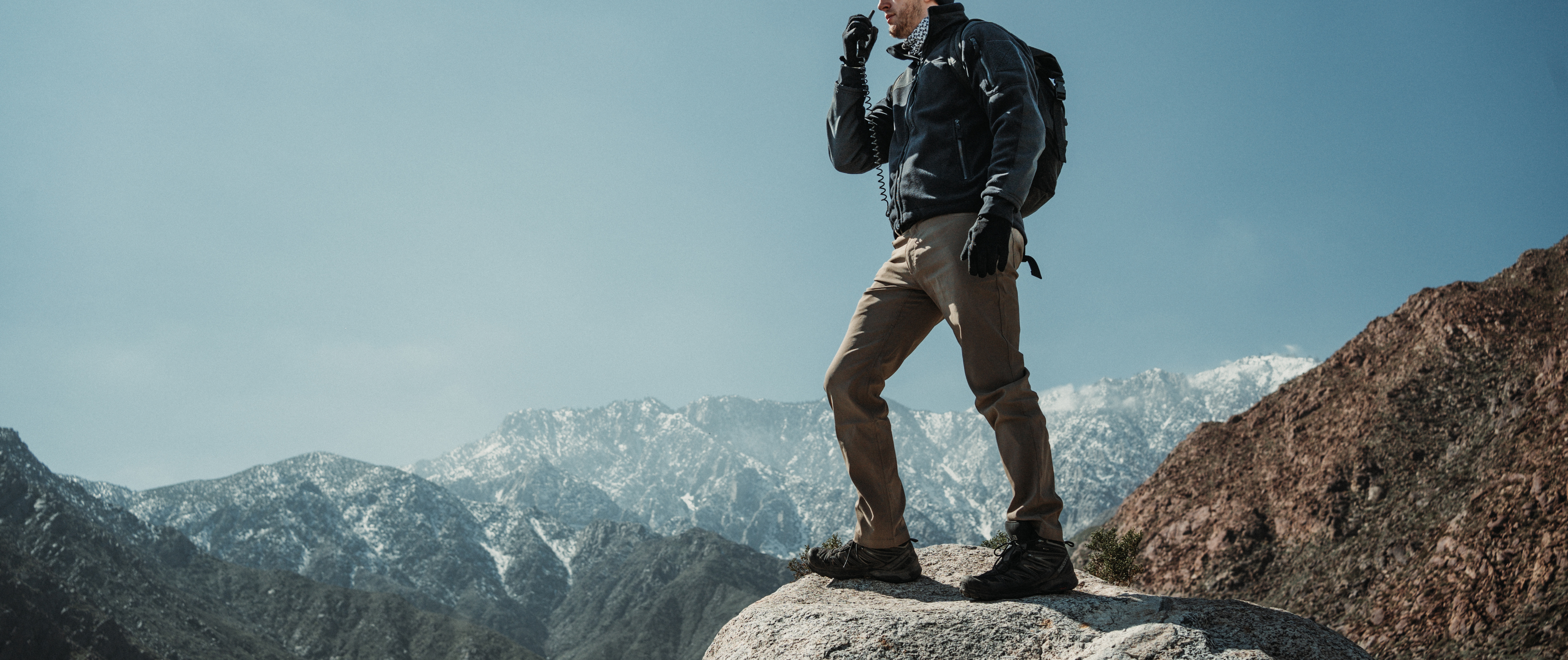 man standing on a rock using a walkie talkie in an alpha fleece jacket and cipher pants