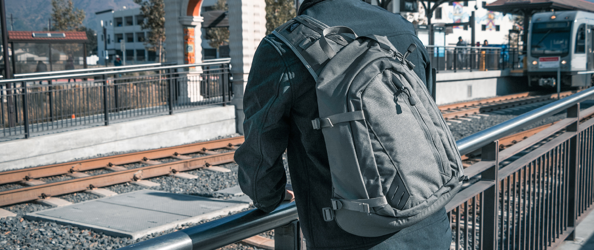 a person standing by railroad tracks wearing the sector sling pack