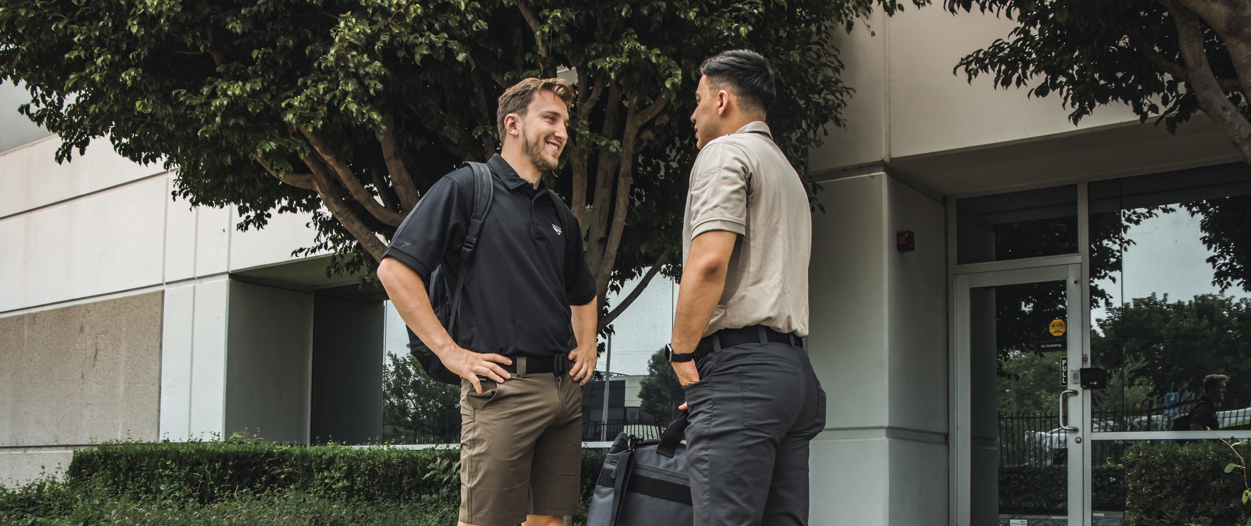 image of two workers talking outside of an office in performance tactical polo shirts