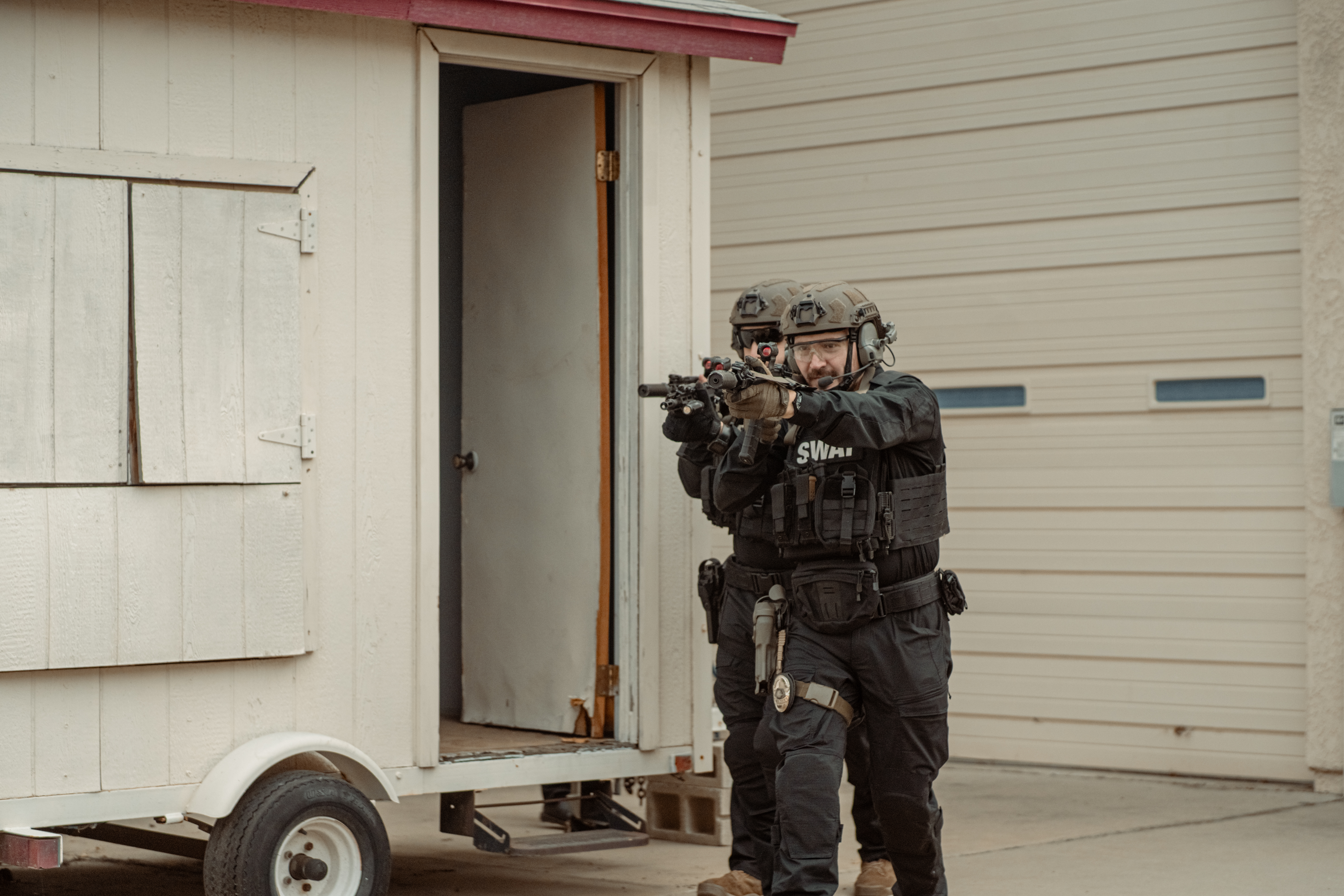 Image of two officers advancing with their rifles pointed. The lead man is wearing a waist pack on his carrier. 